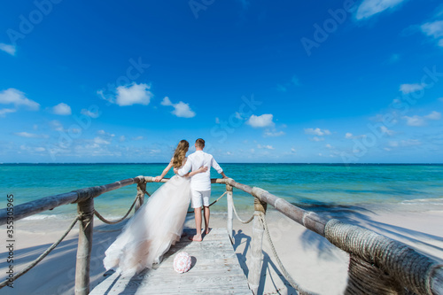 Canvas Print Newlyweds holding hands hugging at white sandy tropical caribbean beach landscap
