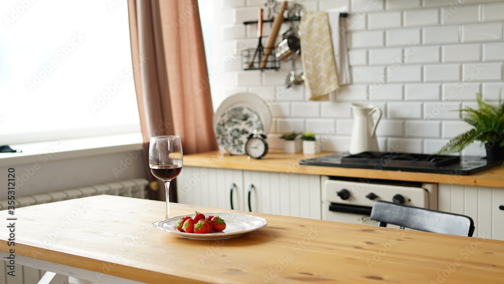 Close up of glass of wine with strawberries on plate on table in kitchen. Concept of dating.