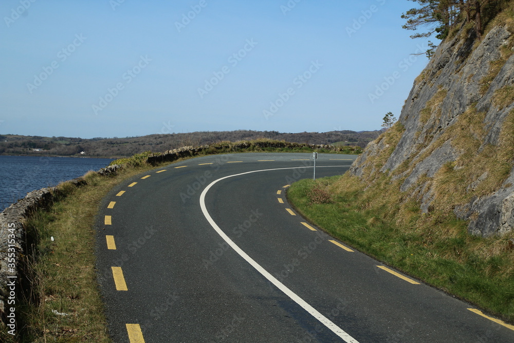 Regional road  with sweeping right bend located between rock face and lake, Dromahair, County Leitrim, Ireland