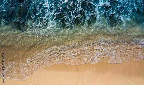 Drone view directly above of tidal waves splashing along a white sand beach. Image taken in Bali Indonesia.