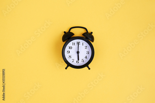 View from above on black alarm clock on yellow background. 6 a.m. Time is now