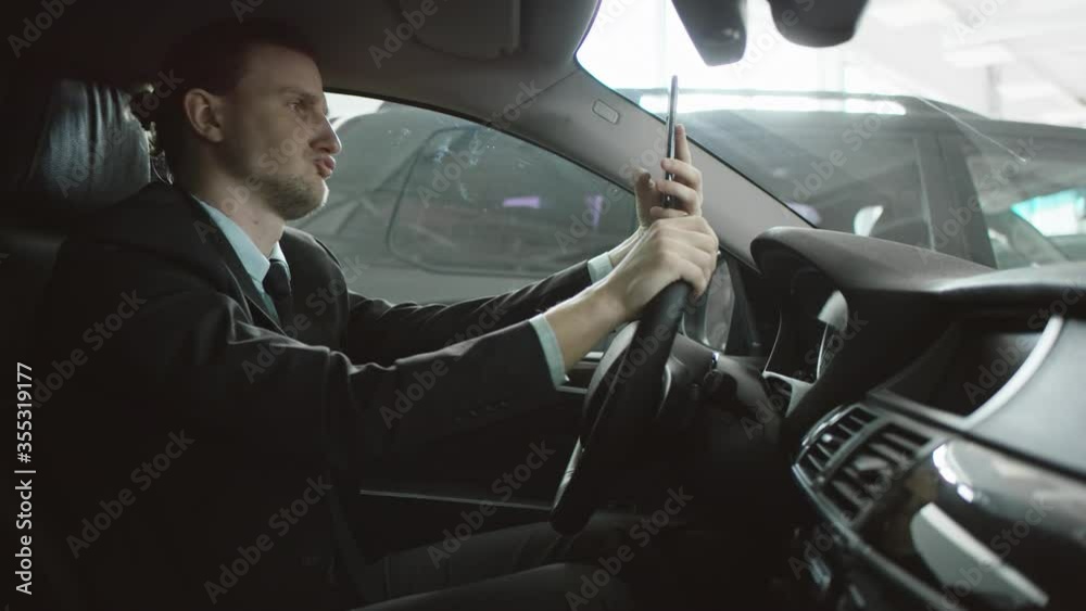 Man is making selfies sitting in the car on a driver's seat and using his phone. Businessman talking while sitting in a car. Man is making selfies sitting in the car on a driver's seat and using his phone. Businessman talking while sitting in a car.