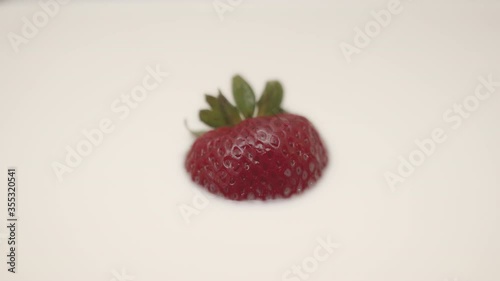 High quality close-up 4k slow motion video of a one strawberry falling into the vegan almond creamy coloured milk