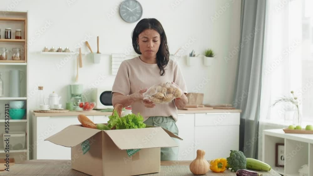 Medium shot of young mixed-race woman unpacking delivered box with food and commenting her actions on camera