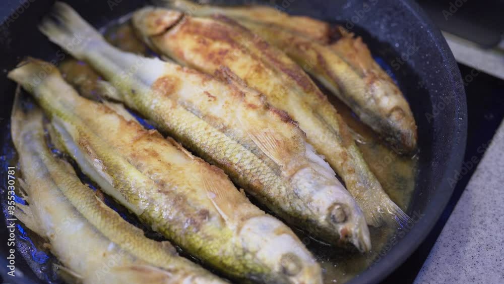 Smelt fish is fried in oil in a black pan. Close-up shot. Seafood cooking Smelt fish is fried in oil in a black pan. Close-up shot. Seafood cooking