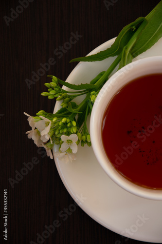  black tea in a white mug on a white saucer decorated with a sprig of wild white flowers on a dark background