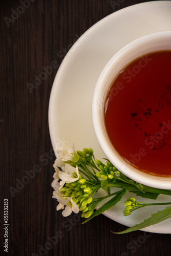  black tea in a white mug on a white saucer decorated with a sprig of wild white flowers on a dark background
