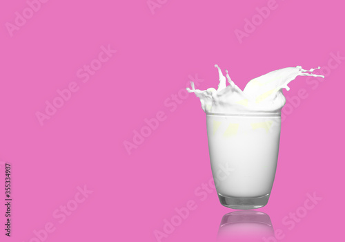 white milk big splash in clear glass on pink background