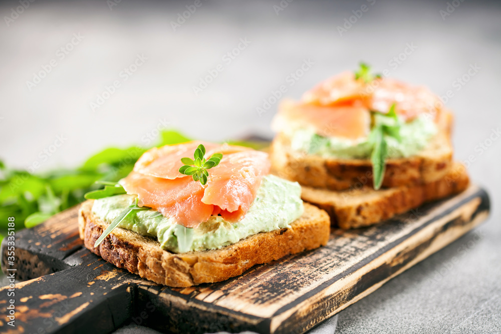 Green cream cheese, salmon and arugula sandwich on a wooden board. Smorrebrod Green cream cheese, salmon and arugula sandwich on a wooden board. Smorrebrod