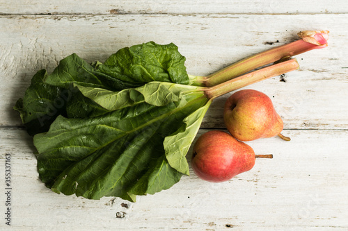 Rhubarb stalks and two pears on a white wooden background. Complementary colors. Grass and fruit. Horizontal orientation