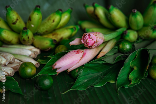 Asian food ingredients such as lemongrass, calamansi, tumeric leaves, torch lily and bananas on a banana leaf background.
