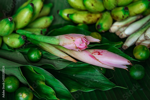 Asian food ingredients such as lemongrass, calamansi, tumeric leaves, torch lily and bananas on a banana leaf background.