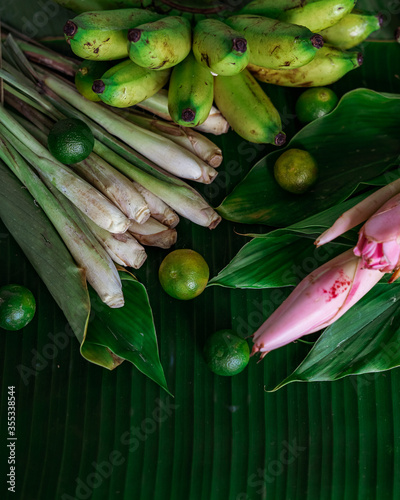 Asian food ingredients such as lemongrass, calamansi, tumeric leaves, torch lily and bananas on a banana leaf background.