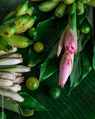 Asian food ingredients such as lemongrass, calamansi, tumeric leaves, torch lily and bananas on a banana leaf background.