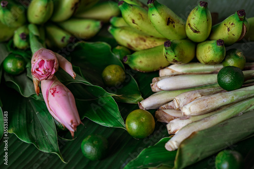 Asian food ingredients such as lemongrass, calamansi, tumeric leaves, torch lily and bananas on a banana leaf background.