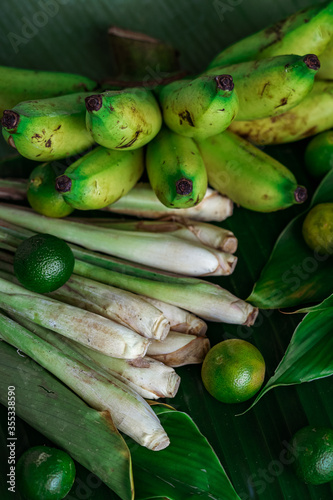 Asian food ingredients such as lemongrass, calamansi, tumeric leaves, torch lily and bananas on a banana leaf background.