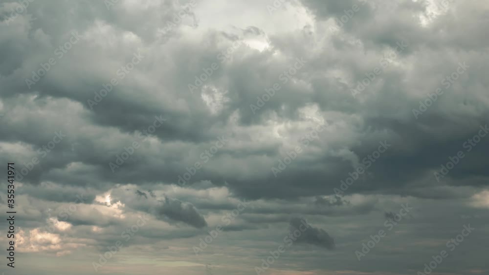 Aerial zoom out cloudscape cloudy sky timelapse over the water of Lake Michigan as a storm blows through at dusk just before the sun sets creating orange colored clouds on a blue sky.