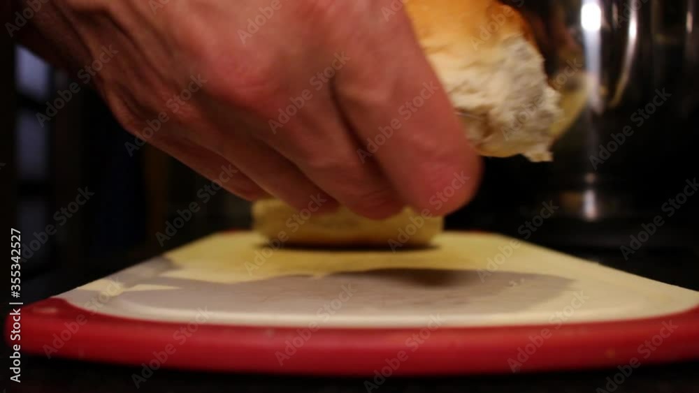 A man cutting two burger buns on a chopping board in a kitchen at night time A man cutting two burger buns on a chopping board in a kitchen at night time