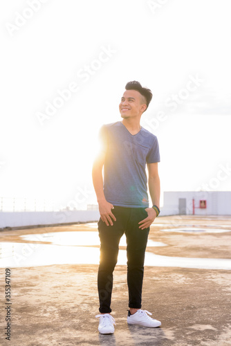 Full body shot of happy young multi ethnic man thinking at rooftop of the building