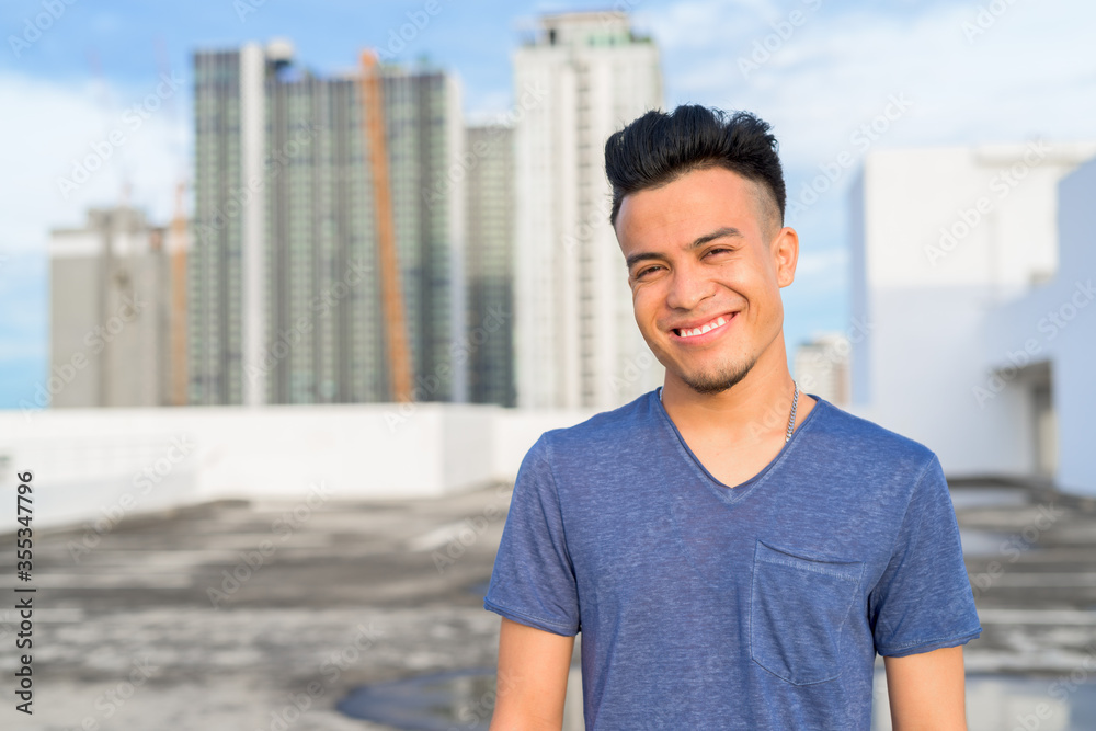 Happy young handsome multi ethnic man smiling against view of the city Happy young handsome multi ethnic man smiling against view of the city