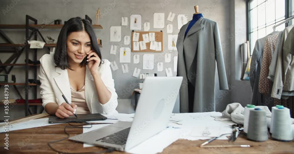 Asian female fashion designer working in her office, drawing sketches on graphics tablet while dialing or recording voice message for customer - fashion concept 4k footage