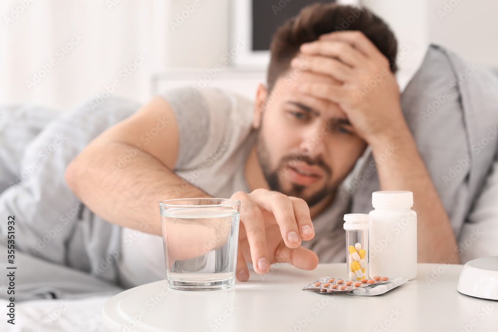 Man taking sleeping pills from table in bedroom Man taking sleeping pills from table in bedroom