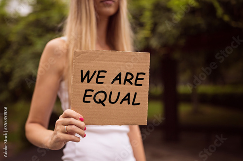 Gender equality concept as woman hands holding a paper sheet with inscription We are equal. Woman protesting outdoor. Metaphor of social issue.