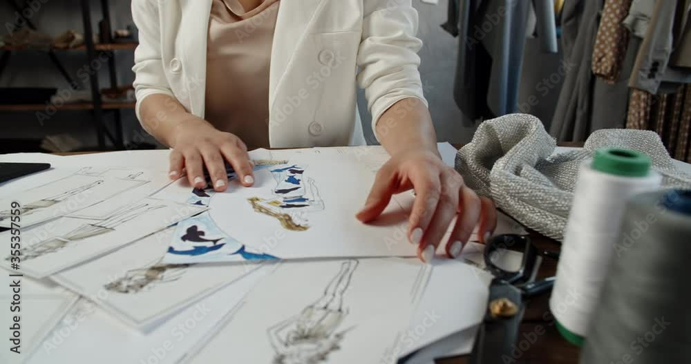 An unrecognizable tailor is working at her office, drawing sketches from paper to graphics tablet, working on her new collection - fashion concept 4k footage close up