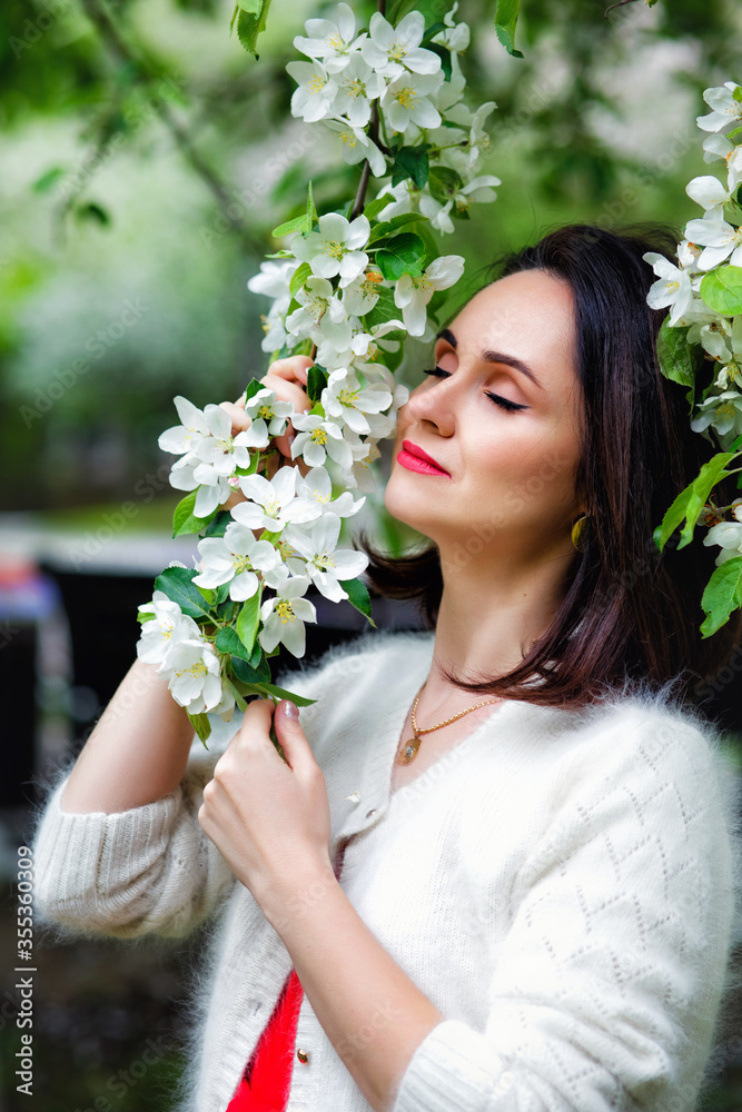Brunette in flowers. The girl hugs a large bouquet of white flowers and smiles with her eyes closed. A young woman in flowers with her eyes closed. One-stop blooming in the spring Brunette in flowers. The girl hugs a large bouquet of white flowers and smiles with her eyes closed. A young woman in flowers with her eyes closed. One-stop blooming in the spring