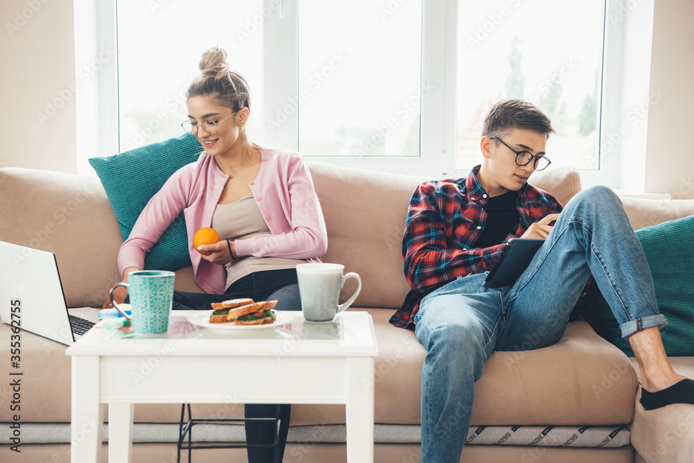 Business couple working at laptop while sitting in sofa and drinking tea with sandwiches Business couple working at laptop while sitting in sofa and drinking tea with sandwiches