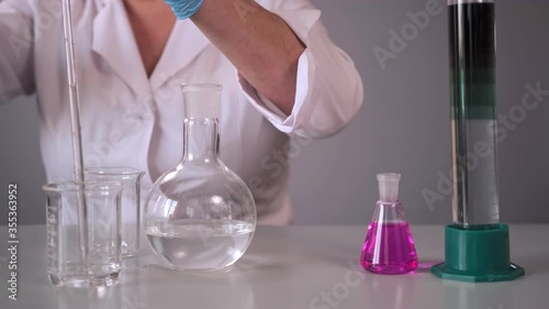 Female hands of a scientist perform an experiment using reagents in the laboratory. A woman mixes liquids in a laboratory flask that change color. Beautiful experience with liquid.