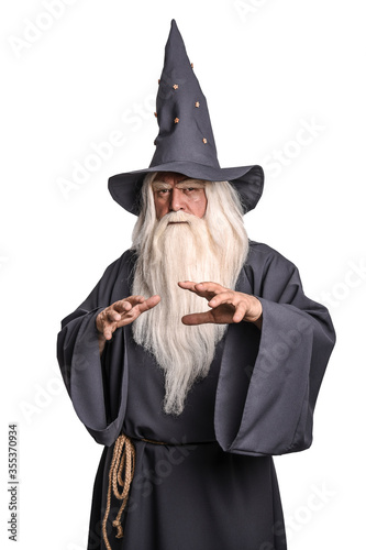 A stern grey-haired bearded wizard in a gray cassock and a cap is practicing sorcery, doing magic against a white insulating background. photo