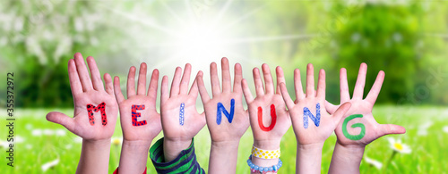 Children Hands Building Colorful German Word Meinung Means Opinion. Sunny Green Grass Meadow As Background