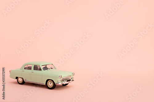 Green retro toy car delivering flowers and gifts on a pink background. Copy space.