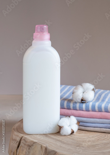 One bottle of white fabric softener, stack of towels on light background. Laundry day