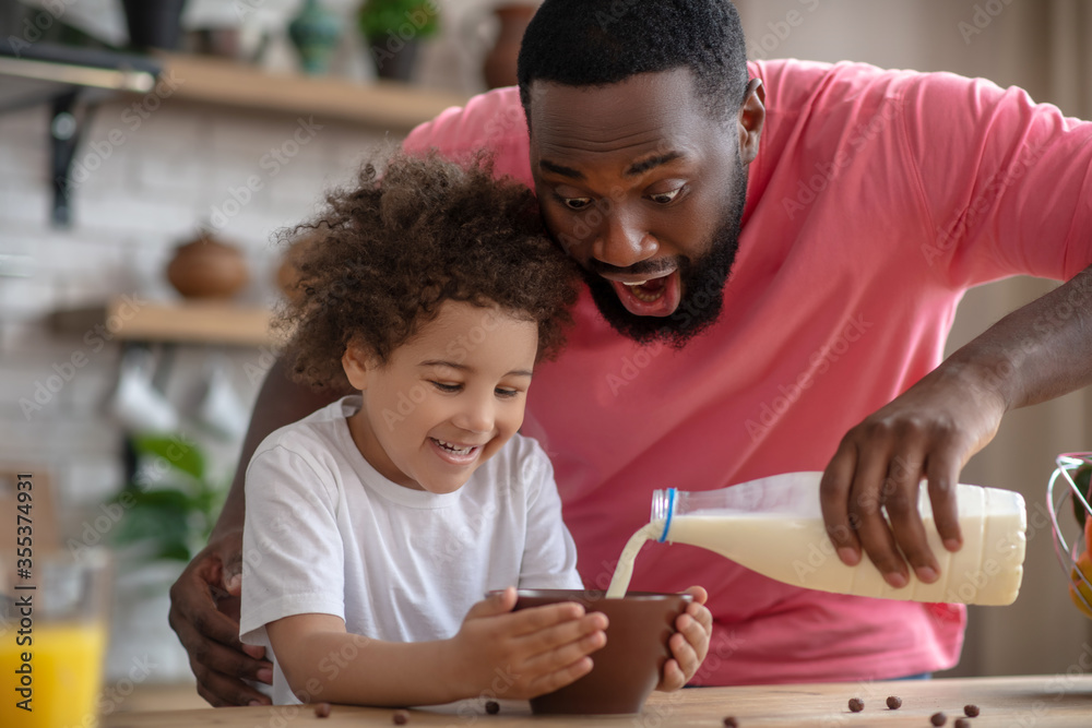 African american bearded man pouring milk in his daughters plate African american bearded man pouring milk in his daughters plate
