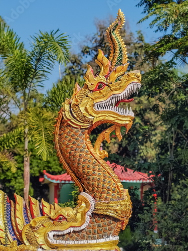view of golden Naga sculpture  Phraya Nak or Dragon in Chinese  with green nature blurred background.