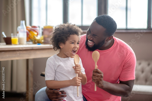 Foto Cute kid with curly hair and her father holding spoons and singing a song