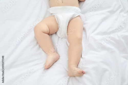 Cute little baby in diaper on bed, top view