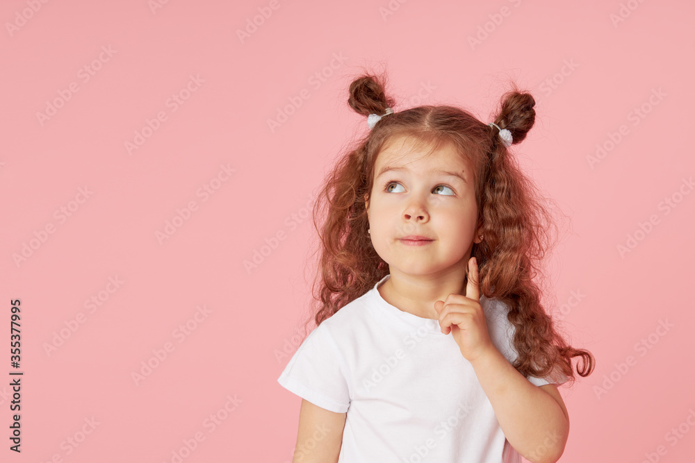 Portrait of surprised cute little toddler girl child over pink background. Looking at camera. Points hands to the left side. Advertising childrens products Portrait of surprised cute little toddler girl child over pink background. Looking at camera. Points hands to the left side. Advertising childrens products