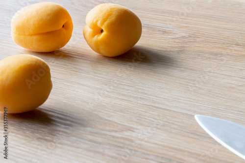 three apricots and knife in backlight on a wooden background