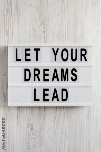 'Let your dreams lead' on a lightbox on a white wooden surface, overhead view. Flat lay, top view, from above.