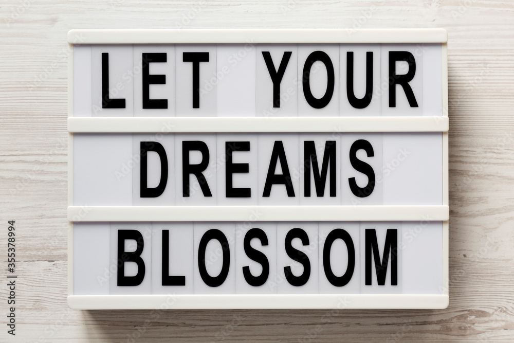 'Let your dreams blossom' on a modern board on a white wooden background, top view. Flat lay, overhead, from above.