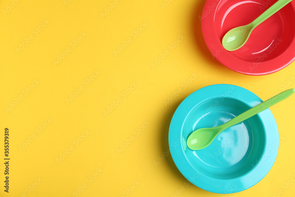 Set of colorful plastic dishware on yellow background, flat lay with space for text. Serving baby food Set of colorful plastic dishware on yellow background, flat lay with space for text. Serving baby food