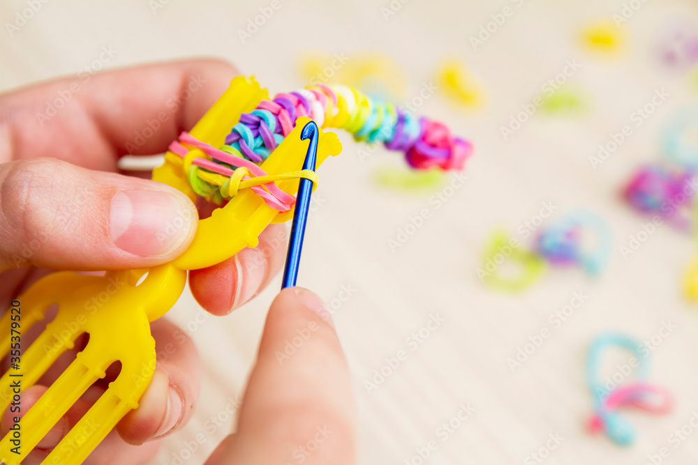 Rubber Band Weaving. Knitting rubber bands with loom knit. Hands of girl weaving wristband of