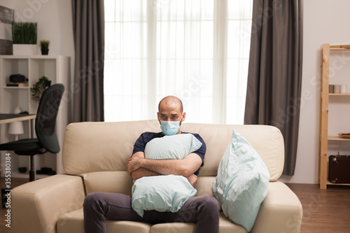 Man holding a pillow in arms while sitting depressed on the couch because of self isolation.