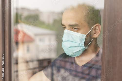 Serious man looking outside through windos glass during quarantine wearingglass d photo