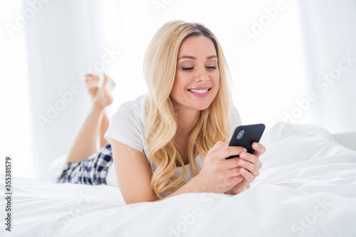 Closeup photo of pretty house wife lady hold telephone writing blog social network post lying cosy bed freelancer quarantine white linen warm sunny morning stay home wear pajama room indoors