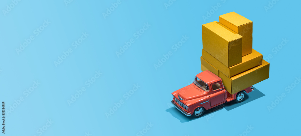 Fast order delivery by car concept. Pickup truck delivering blank boxes. Loaded retro toy car loaded with cardboard packages isolated on blue background. Fast order delivery by car concept. Pickup truck delivering blank boxes. Loaded retro toy car loaded with cardboard packages isolated on blue background.