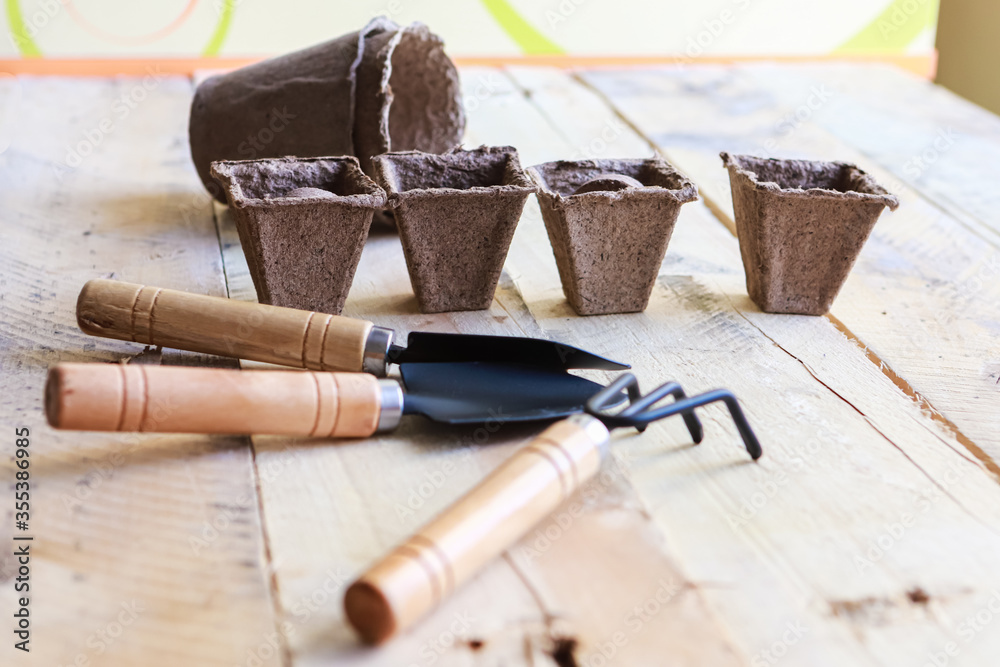 Naklejka premium Biodegradeble pots, rake and spade on wooden background. Garden tools.